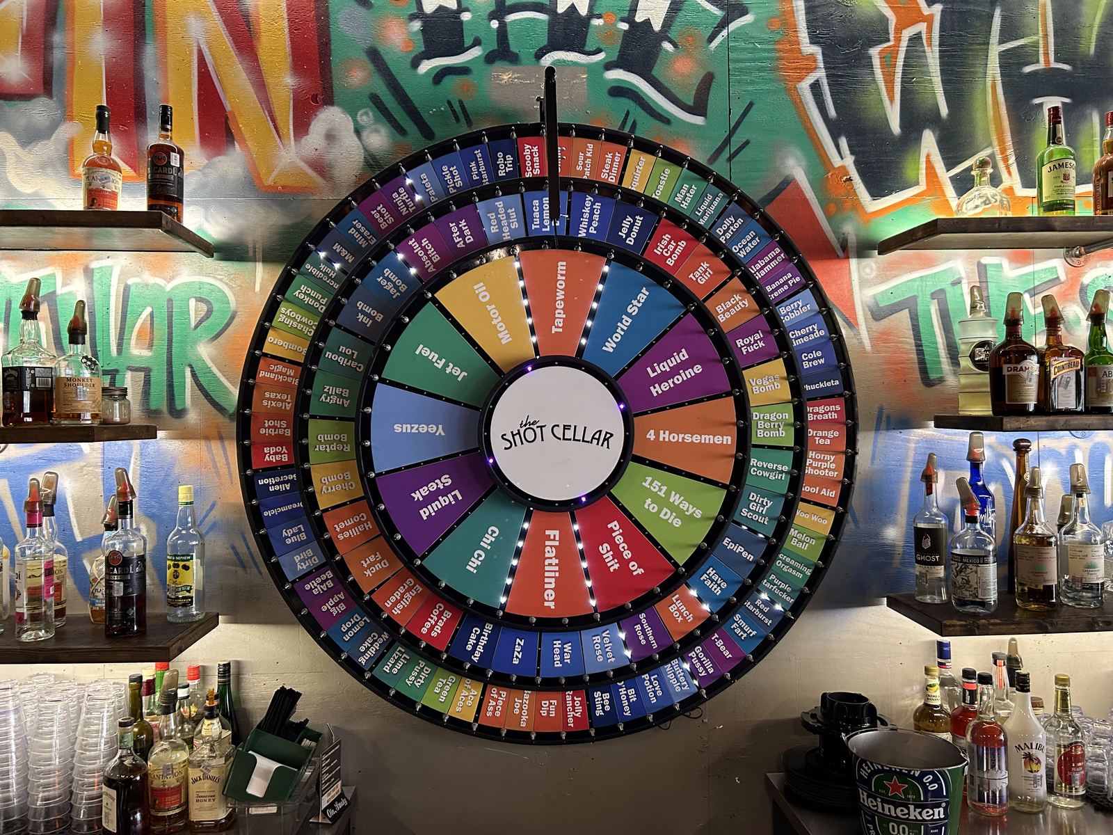 The Shot Cellar's three-tier shot wheel on the wall behind the bar, photographed from below against a painted mural